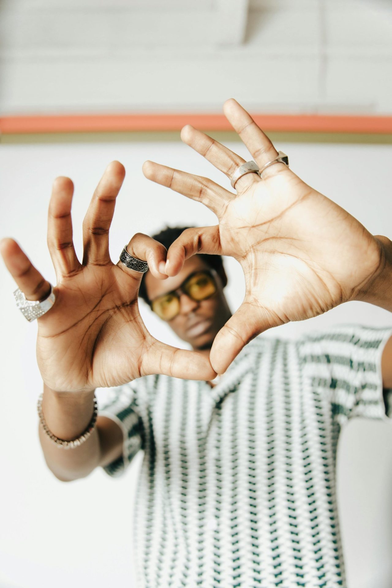 Young man making a heart shape with hands, wearing sunglasses, showcasing unique rings.