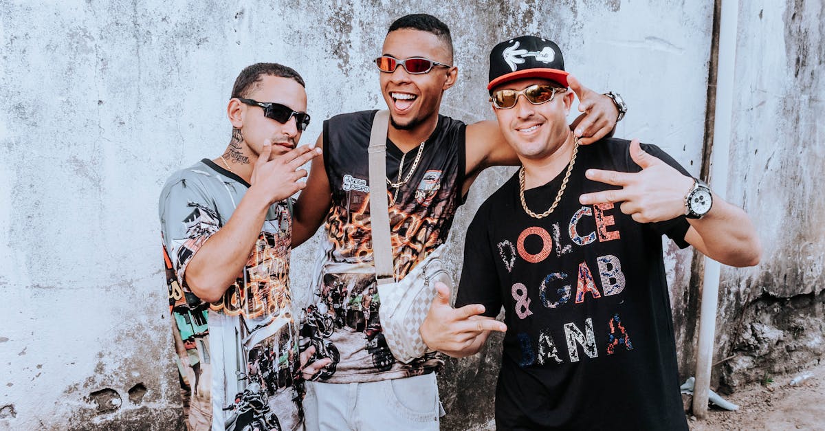 Three urban musicians posing energetically against a rustic wall, showcasing streetwear fashion.